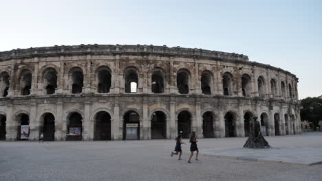 Pan-right-shot-of-Arena-of-Nimes,-children-running-up-to-Nimeno-II-statue