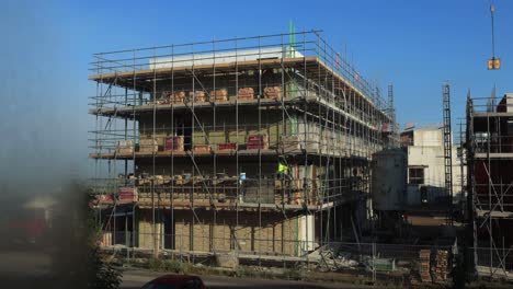 Zeitraffer-Auf-Der-Baustelle-Mit-Vernebelter-Sicht-Und-Vorbeiziehender-Wolkendecke-Im-Hintergrund-Mit-Arbeitern,-Die-Ziegel-Der-Außenfassade-Verlegen