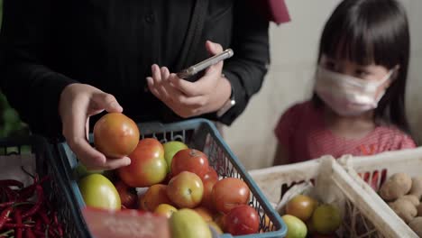 Tomato-shopper-picking-fresh-tomatoes-at-a-traditional-Indonesian-market-with-a-girl-in-the-background-looking-at-it