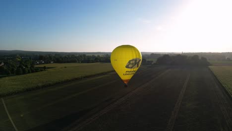 Vista-Aérea-Del-Amanecer-De-La-Mañana-De-Un-Globo-Aerostático-Amarillo-Brillante-Que-Vuela-Sobre-Un-Campo-Rural-En-Los-Países-Bajos