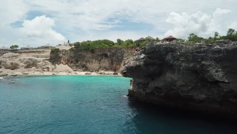 Young-male-does-backflip-off-high-rock-cliff-into-tropical-water-below