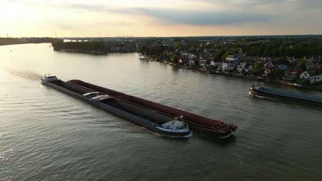 Vista-Aérea-Sobre-El-Carguero-De-Empuje-Amoureus-Navegando-A-Lo-Largo-De-Beneden-Merwede-Durante-La-Puesta-De-Sol-Pasando-Otro-Barco