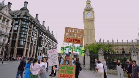 Old-male-climate-activist-in-Westminster,-London,-holding-up-climate-change-and-anti-plastic-signs-to-protest-against-CO2-pollution-and-the-climate-crisis-and-for-nature-protection-and-preservation