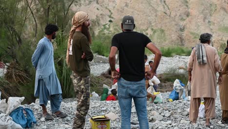 Back-view-of-two-men-talking-to-each-other-standing-beside-other-men-while-standing-on-the-rocky-and-broken-terrain-in-Balochistan,-Pakistan