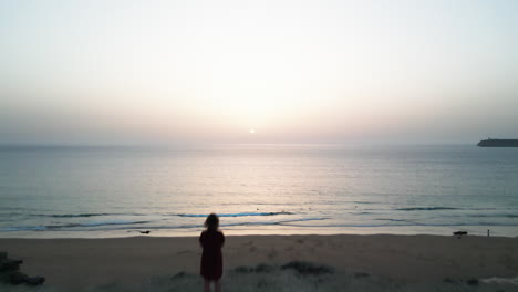 Drone-flying-over-a-woman-standing-on-a-cliff-looking-at-the-ocean