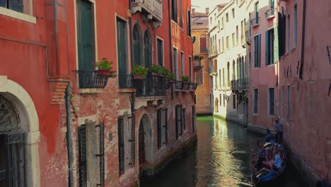 A-canal-in-Venice,-Italy-with-a-gondola-boat,-gondoliere-and-tourists,-old-houses-and-a-cathedral-church-close-to-San-Marco-and-Rialto-Bridge