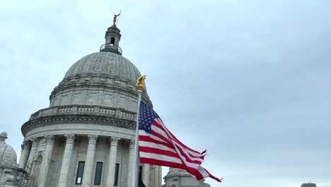 Ondas-De-La-Bandera-Estadounidense-Frente-A-La-Cúpula-Del-Edificio-Del-Capitolio-Estatal-En-Providence,-Rhode-Island