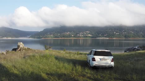 Vista-Aérea-Escénica-Del-Coche-Todoterreno-Mercedes-Blanco-Estacionado-A-Orillas-Del-Lago-Mavrovo-En-Macedonia