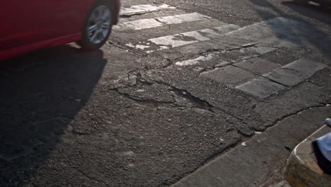 Pedestrians-and-cars-cross-a-crackled-and-damaged-asphalt-street-during-the-afternoon-in-Santa-Ana,-El-Salvador