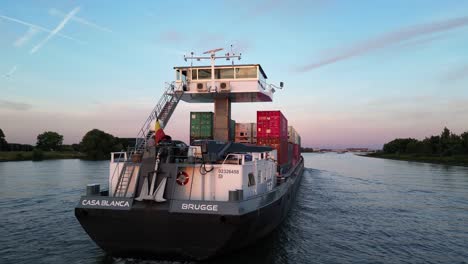 Slide-and-pan-footage-of-container-ship-with-cargo-slowly-moving-on-river-at-twilight