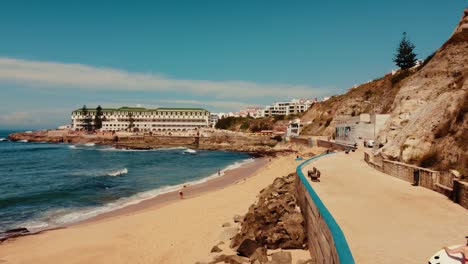 Gente-Disfrutando-Del-Verano-En-La-Playa-De-Foz-Do-Lizandro,-Resort-De-Lujo-En-El-Fondo,-Portugal