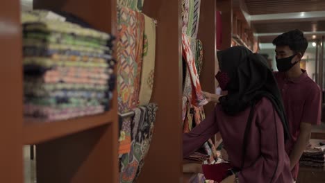 Un-Turista-Asiático-Familiar-Que-Elige-Una-Camisa-De-Batik-De-Una-Fila-De-Varios-Patrones-De-Batik-Colgados-En-Un-Mercado-Local