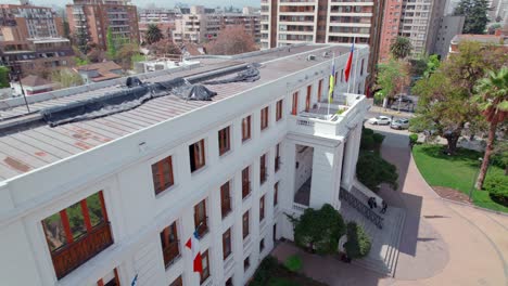 Aerial-view-of-the-building-of-the-municipality-of-Ñuñoa,-Chile-with-the-flag-in-front,-sunny-day