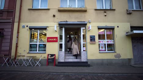 two-girls-in-coats-enters-an-old-shoe-store-with-a-snacks-bar-outside