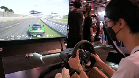 Ein-Chinesischer-Spieler-Spielt-Ein-Themenorientiertes-Rennvideospiel,-Während-Besucher-Das-Hong-Kong-Computer-And-Communication-Festival-In-Hong-Kong-Besuchen