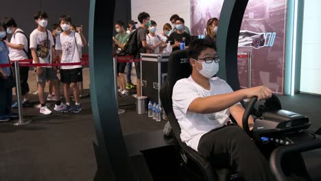 Ein-Chinesischer-Spieler-Spielt-Ein-Themenorientiertes-Rennvideospiel,-Während-Besucher-Und-Enthusiasten-Während-Des-Hong-Kong-Computer-And-Communication-Festival-In-Hong-Kong-Darauf-Warten,-An-Die-Reihe-Zu-Kommen