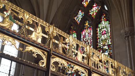 Wells-Cathedral-architecture,-gold-stripe-with-figures-of-people-praying,-stained-glass-windows-in-the-background