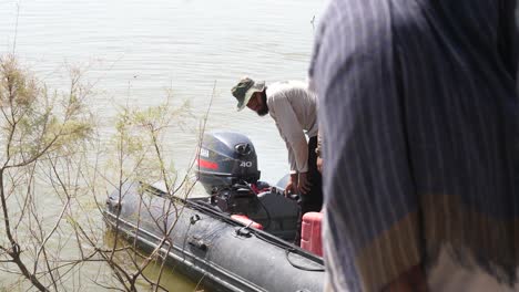 Macho-Pakistaní-Comprobando-El-Motor-De-Un-Bote-Inflable-En-Sindh,-Pakistán