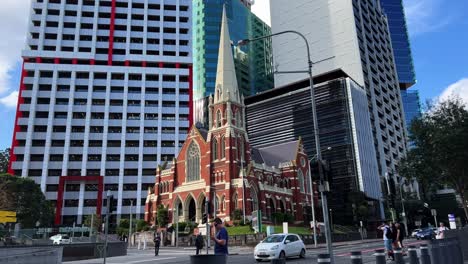 Downtown-Brisbane-city,-pedestrians-crossing-the-street,-cars-driving-pass-heritage-listed-Victorian-Gothic-Revival-architecture,-Albert-street-uniting-church-in-the-background,-static-shot
