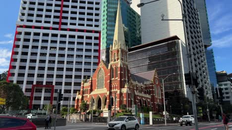 Cars-driving-on-street-with-heritage-listed-Victorian-Gothic-Revival-architecture,-Albert-street-uniting-church-and-modern-high-rise-skyscrapers-at-the-background