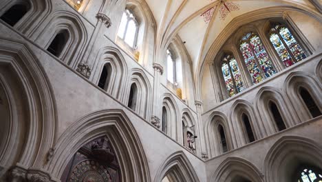 Wells-Cathedral-ceiling-arches,-camera-moving-down-and-rotating-to-the-right-showing-the-tainted-glass-windows-and-finishing-in-the-old-wall-clock