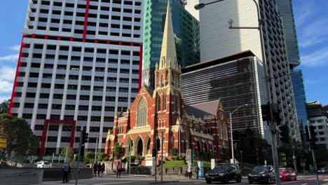 Downtown-Brisbane-city,-pedestrians-crossing-the-street-and-cars-waiting-at-traffic-lights-with-heritage-listed-Victorian-Gothic-Revival-architecture,-Albert-street-uniting-church-in-the-background