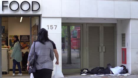 Un-Hombre-Sin-Hogar-Durmiendo-Afuera-De-Una-Tienda-De-Comida-Con-La-Palabra-Comida-En-La-Foto