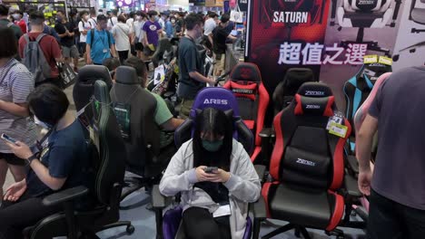 Chinesische-Besucher-Und-Einkäufer-Von-Technologie-Im-Einzelhandel-Stöbern,-Testen-Und-Kaufen-Gaming-Stühle-Während-Eines-Computer--Und-Kommunikationsfestivals,-Während-Käufer-Nach-Ermäßigten-Markenprodukten-Für-Elektronik-Und-Zubehör-Suchen