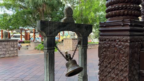 Handheld-shot-capturing-carved-timber-details-of-three-story-high-heritage-building-nepalese-pagoda-with-bronze-bell-ringing-and-swinging-outside-the-main-entrance,-Parklands,-South-Bank-Brisbane-city