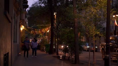 Young-couple-walking-on-the-sidewalk-in-slow-motion-on-a-busy-lighted-street-at-night