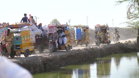 Tuk-Tuks-Amarillos-Pasando-Por-Una-Estrecha-Carretera-Rural-Al-Lado-Del-Río-En-Sindh