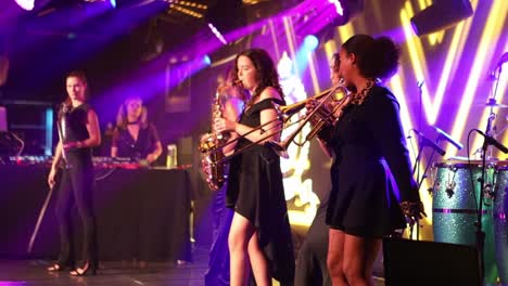 Artistas-Femeninas-En-El-Escenario-Cantando-Y-Tocando-Instrumentos-Durante-Un-Concierto-En-Vivo-Con-Muchas-Luces-De-Colores-En-El-Fondo-En-Londres,-Reino-Unido