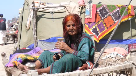 Old-Pakistani-Woman-Flood-Refugee-Sat-On-Bed-Outside-At-Makeshift-Camp-In-Maher,-Sindh,-Pakistan