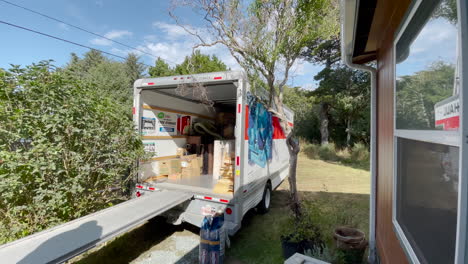 Moving-helpers-carry-boxes-out-of-a-U-Haul-truck-parked-close-to-a-residence