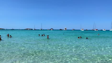 épico-Destino-De-Vacaciones-De-Verano-En-La-Isla-De-Formentera-Ses-Illetes-Playa-Ibiza-España,-Aguas-Turquesas-Transparentes-Y-Yates-De-Lujo-En-Una-Playa-De-Arena-Blanca,-Gente-De-Vacaciones,-4k-Panorámica-A-La-Derecha