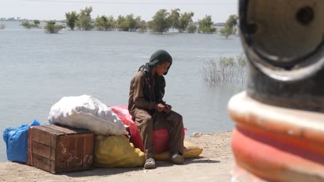 Video-De-Los-Adolescentes-Sentados-En-El-Saco-De-Suministros-Y-Mirando-El-Lago-Que-Fluye-Detrás-De-él-En-Maher,-Sindh