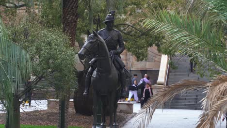 Primer-Plano-De-La-Escultura-Scout,-Memorial-De-Guerra-Sudafricano-En-La-Plaza-Anzac-Con-Trabajadores-De-Oficina-Corriendo-A-Casa-Hacia-La-Estación-De-Tren-Subterráneo-En-El-Distrito-Central-De-Negocios,-Ciudad-De-Brisbane