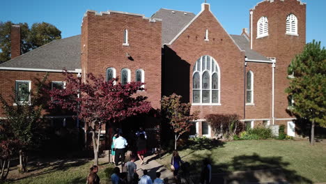 Drone-shot-over-local-people-entering-a-church-in-Tulsa,-Oklahoma,-USA-with-visitors-walking-up-the-stairs-to-enter-the-church-at-daytime