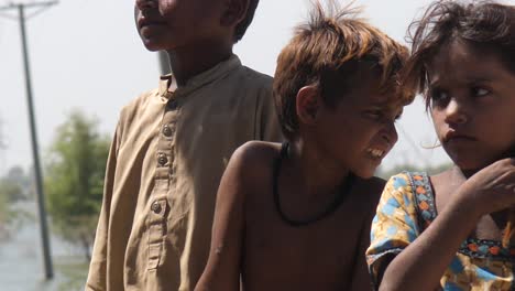 Primer-Plano-De-Dos-Niños-Pobres-Y-Una-Niña-Pequeña-Desnutrida-Que-Están-De-Pie-Bajo-El-Sol-Para-Recibir-Ayuda-Por-Inundaciones-En-Maher,-Sindh