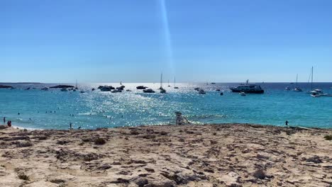 Destino-De-Vacaciones-De-Ensueño-De-Verano-Soleado-En-La-Isla-De-Formentera-Playa-De-Ses-Illetes-Ibiza-España,-Agua-Turquesa-Transparente-Y-Yates-De-Lujo-En-Una-Playa-Rocosa-De-Arena-Blanca,-Gente-De-Vacaciones,-Tiro-De-4k