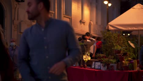 Gente-Caminando-Tranquilamente-A-Cámara-Lenta-Por-La-Noche-En-Una-Calle-Al-Lado-De-La-Terraza-De-Un-Restaurante