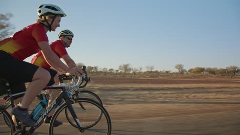 Sideway-tracking-shot-of-a-pair-of-cyclists-waving-to-the-camera