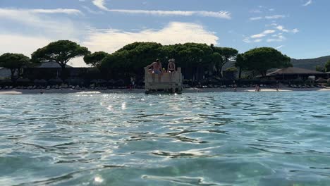 People-sitting-on-edge-of-wooden-pier-of-Santa-Giulia-beach-in-Corsica-island,-France