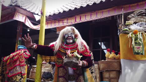 Balinese-Dancer-Wearing-a-Cultural-Mask-Topeng-Sidakarya,-Praying-Dance-in-Bali-carrying-Incense-and-Flowers-Offerings,-Temple-in-Ubud