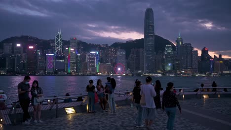 Einheimische-Und-Touristen-Werden-An-Der-Uferpromenade-Von-Victoria-Harbour-Gesehen,-Während-Sie-Den-Nächtlichen-Blick-Auf-Die-Skyline-Der-Wolkenkratzer-Der-Insel-Hong-Kong-Genießen