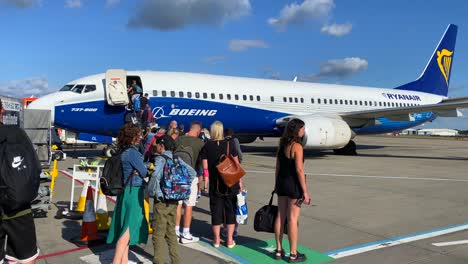 People-waiting-in-line-while-slowly-boarding-a-big-Ryanair-boeing-airplane-in-Bristol-international-airport-on-a-sunny-day,-holiday-vacation-time,-4K-static-shot