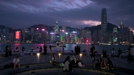 Se-Ve-A-La-Gente-En-El-Paseo-Marítimo-Del-Puerto-Victoria-Mientras-Disfrutan-De-La-Vista-Nocturna-Y-Del-Horizonte-De-Los-Rascacielos-De-La-Isla-De-Hong-Kong