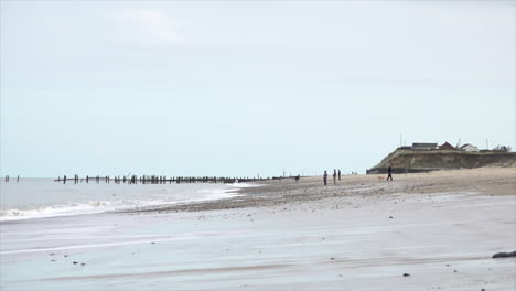 Menschen-Gehen-Am-Strand-Entlang-An-Der-Küste-Von-Norfolk,-Die-Durch-Küstenerosion-Beschädigt-Wurde,-Wenn-Wellen-Von-Der-Nordsee-Hereinrollen