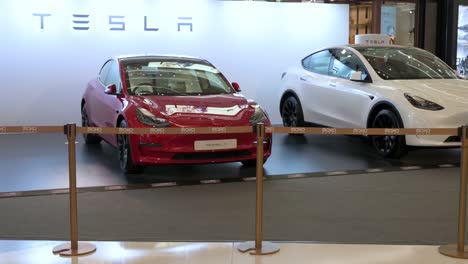 Chinesische-Käufer-Gehen-In-Einem-Einzelhandelseinkaufszentrum-In-Hongkong-Am-Ausstellungsraum-Des-Amerikanischen-Elektroautoherstellers-Tesla-Motors-Vorbei,-In-Dem-Elektrofahrzeuge-Wie-Die-Autos-Der-Modelle-X-Und-Y-Ausgestellt-Sind