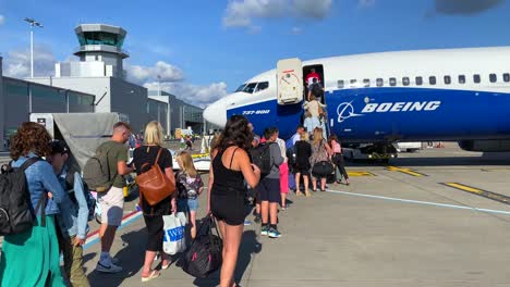 People-waiting-in-line-while-boarding-a-big-Ryanair-boeing-airplane-in-Bristol-international-airport-on-a-sunny-day,-holiday-vacation-time,-4K-static-shot